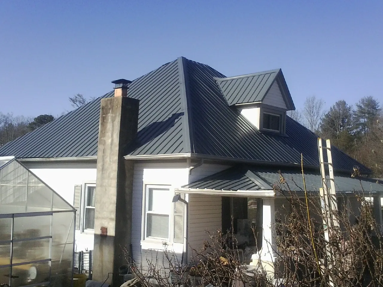 Dark blue standing seam metal roof on a white farmhouse with dormer in Harmony